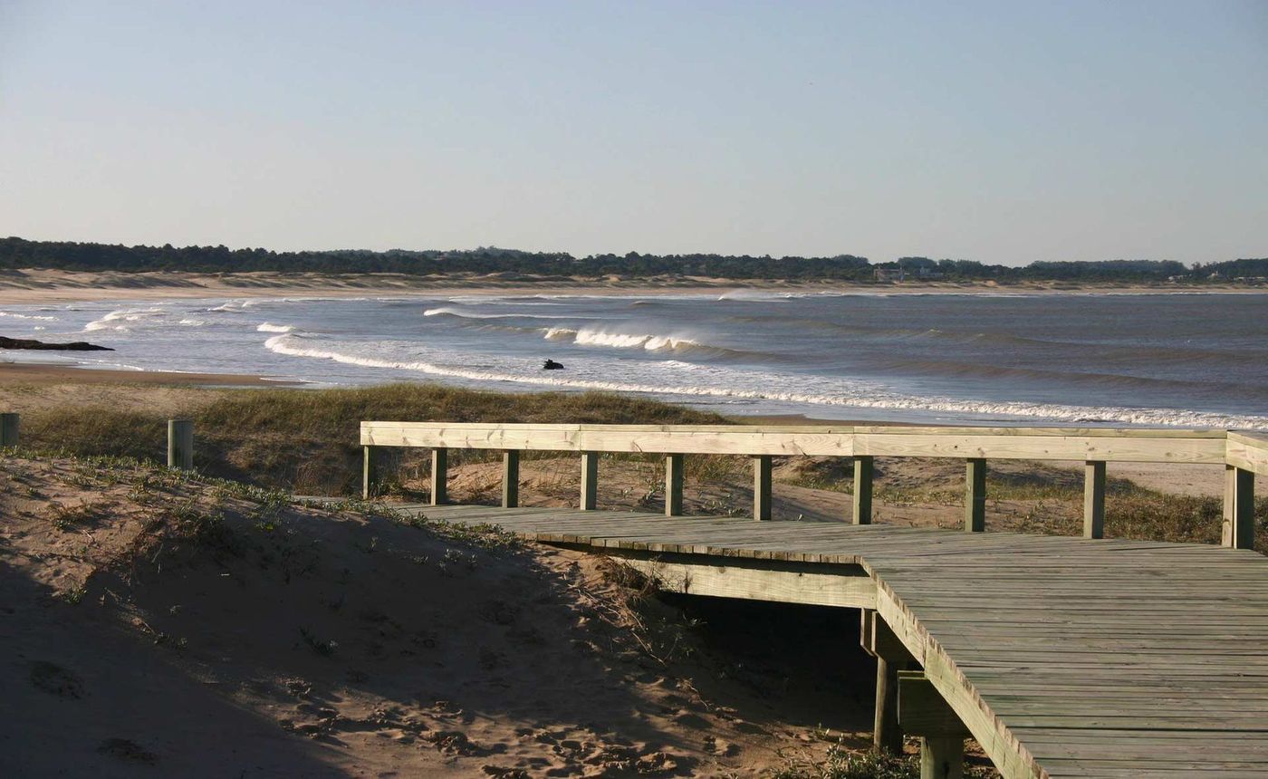 Pasarela de madera bajando a la playa, con las olas rompiendo