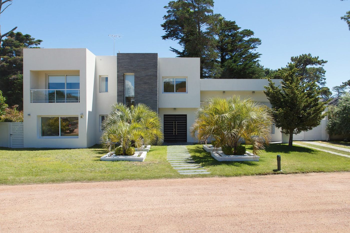 Frente de casa blanca con palmeras butiá y canteros cuidados