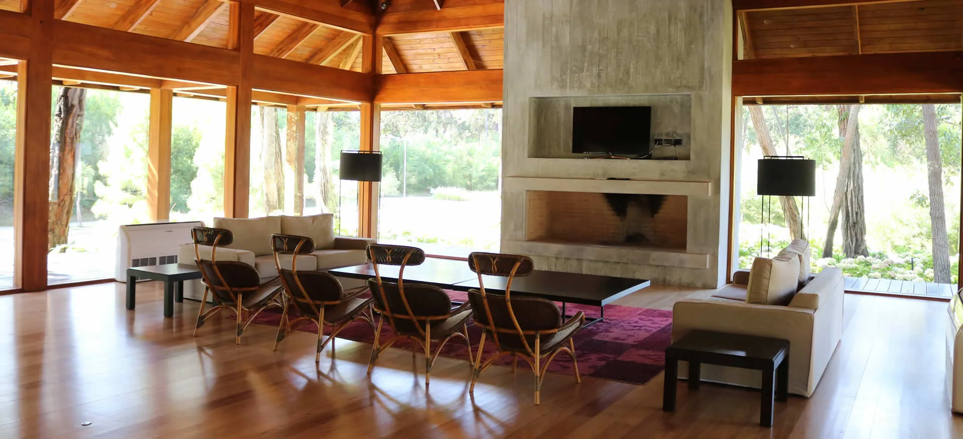 Interior del clubhouse con estructura de madera, estufa y galerías al bosque