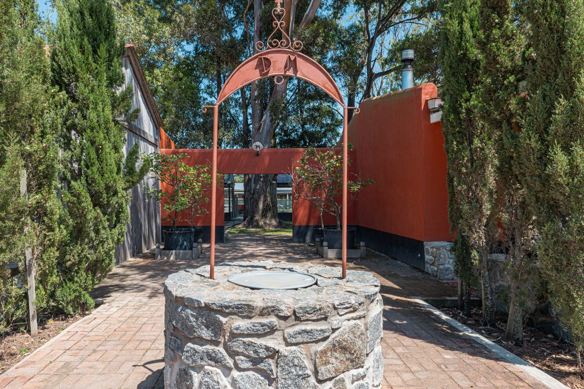 Detalle del aljibe de piedra con el arco de hierro y el monograma del barrio