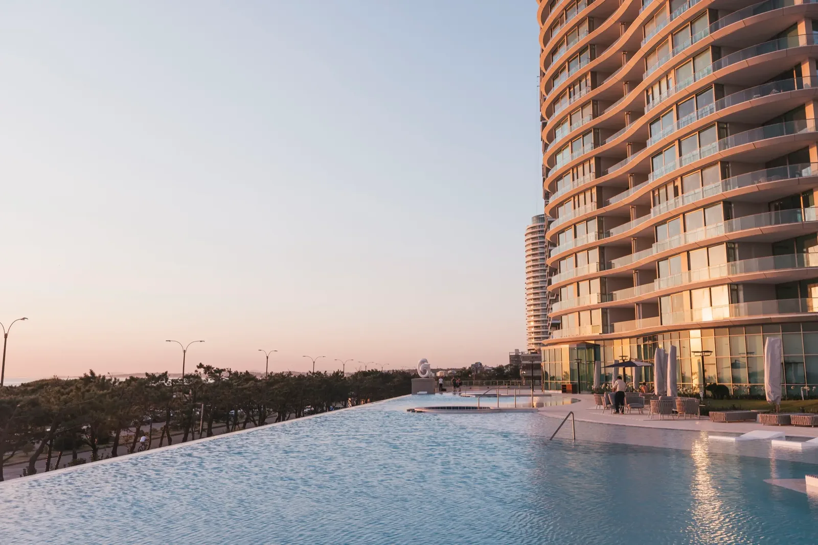 Piscina infinita de Fendi Château al atardecer, con la costa de la Mansa de fondo