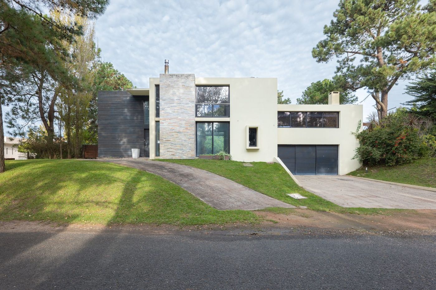 Casa moderna blanca con chimenea de piedra, desde la vereda