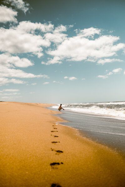 Playa oceánica con huellas en la arena y una persona en la orilla