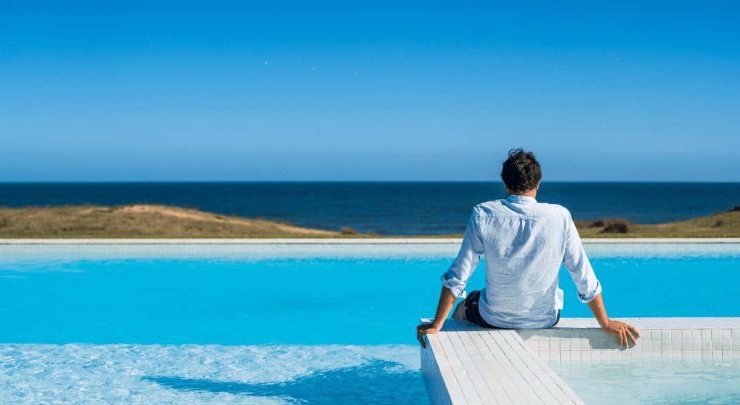 Un hombre al borde de la piscina infinita, con el mar de frente