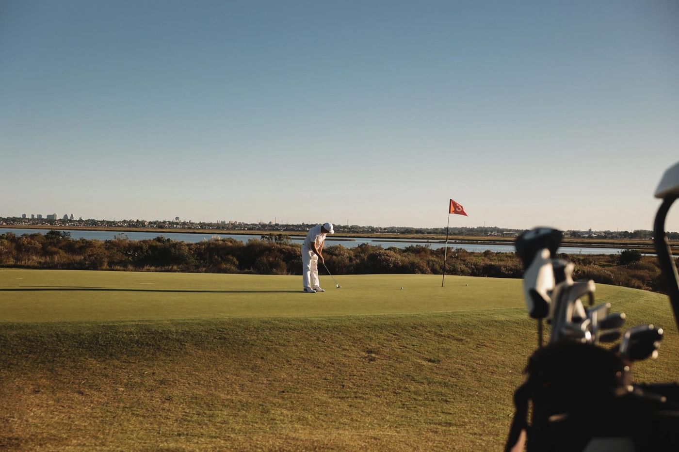 Golfista embocando en el green, con el humedal y Punta del Este en el horizonte