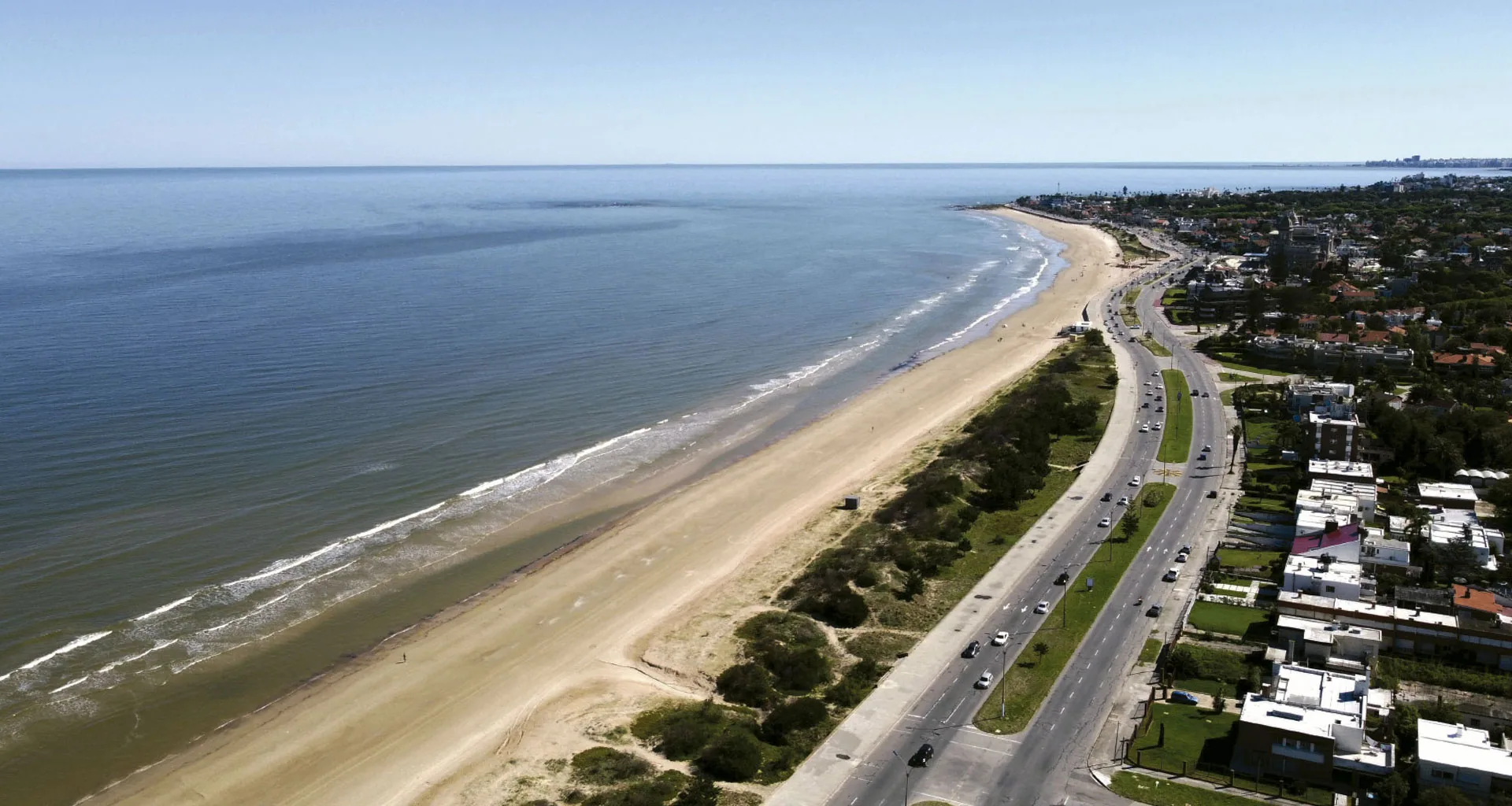 Aérea de una playa larga con avenida costanera y casas