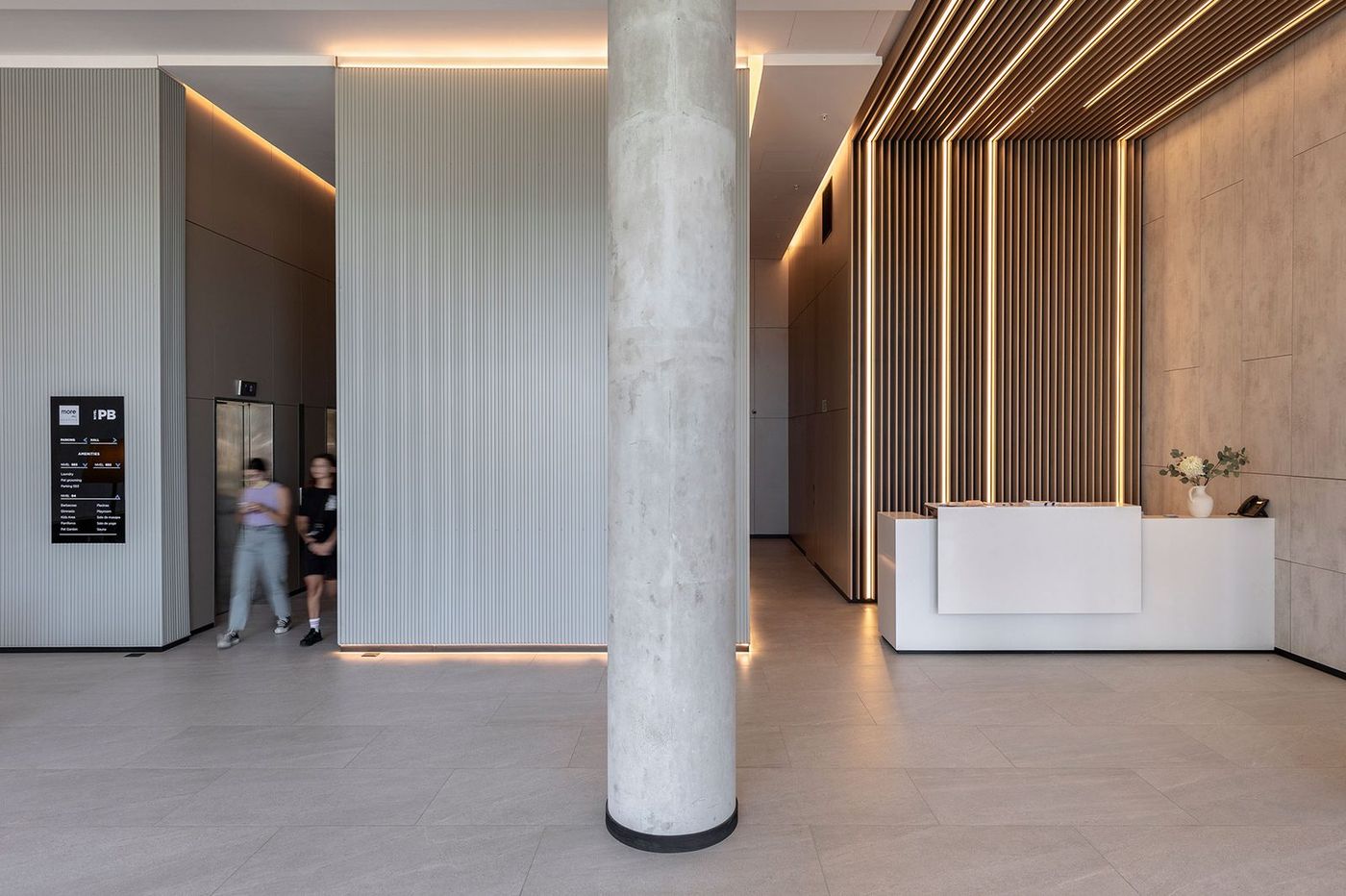 Lobby terminado con la recepción, listones de madera retroiluminados y gente