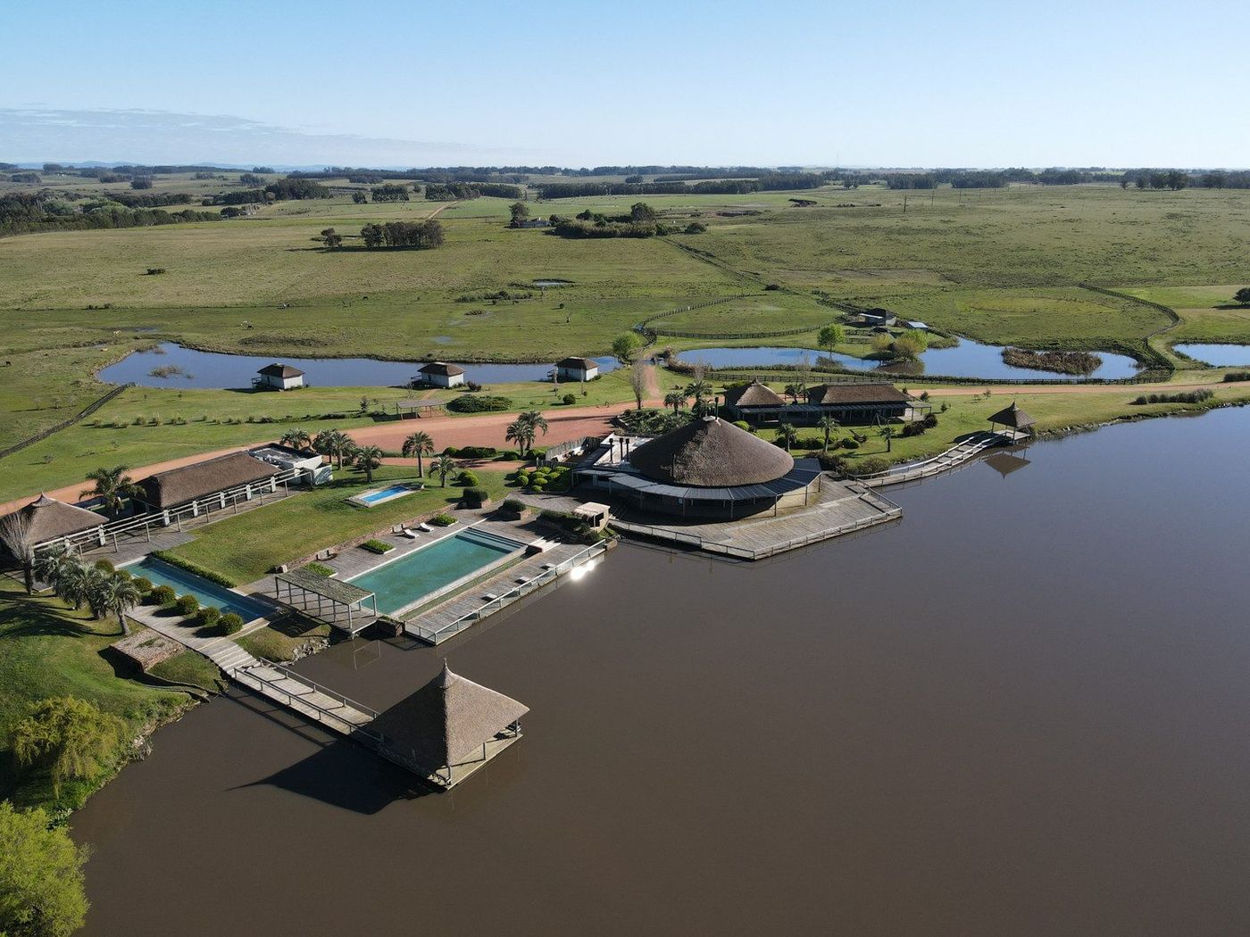 Aérea de la beach house sobre la laguna, con las dos piscinas y el muelle