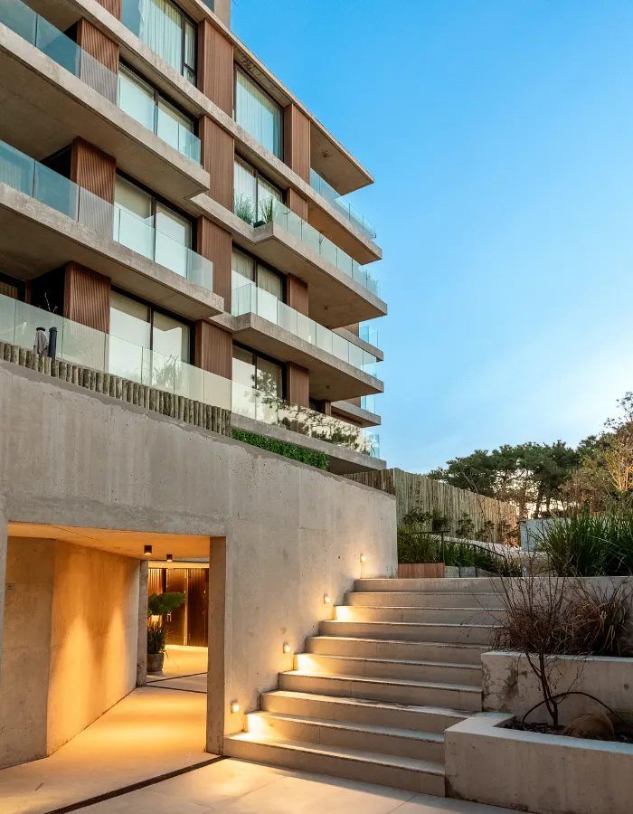 Acceso escalonado iluminado al atardecer, con el edificio arriba