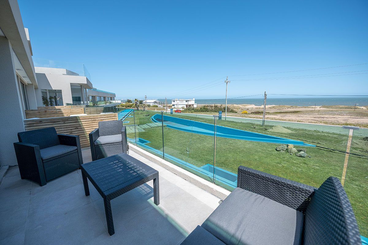 Terraza de una unidad con sillones, las piscinas y el mar de fondo