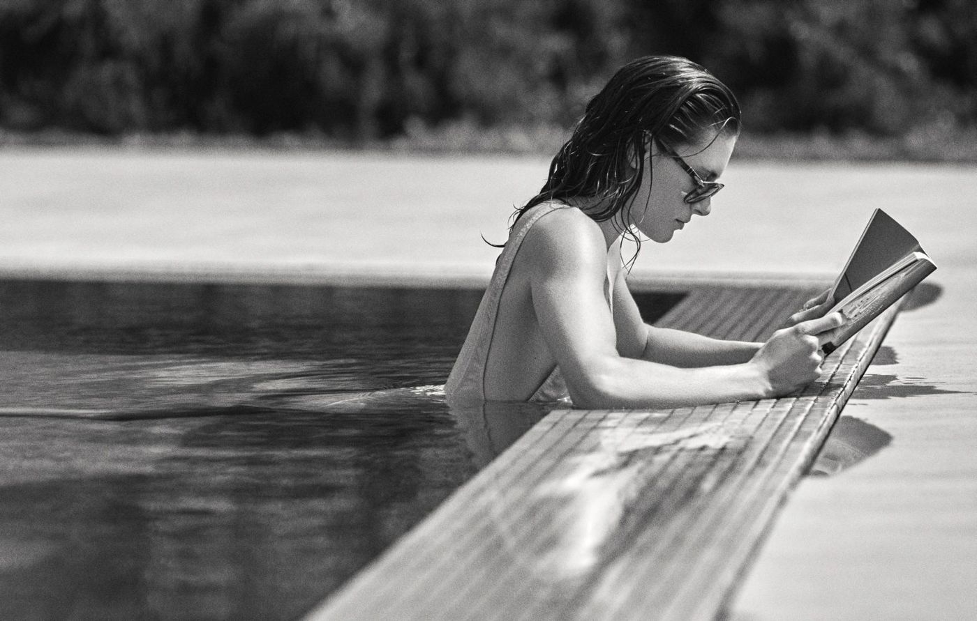 Foto en blanco y negro de una mujer leyendo al borde de la piscina