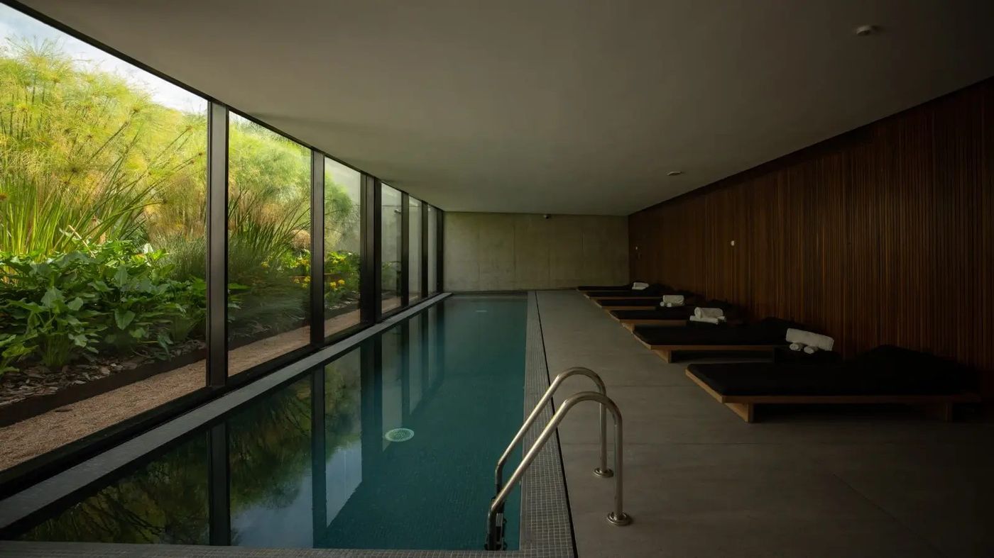 Piscina cubierta en penumbra, con camastros de madera oscura
