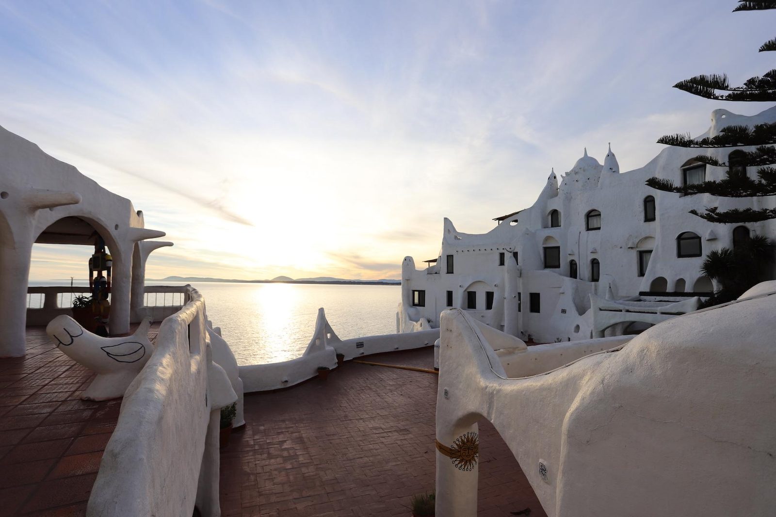 Terraços de Casapueblo ao entardecer, com as esculturas brancas de Páez Vilaró e o sol se pondo sobre a baía de Punta Ballena