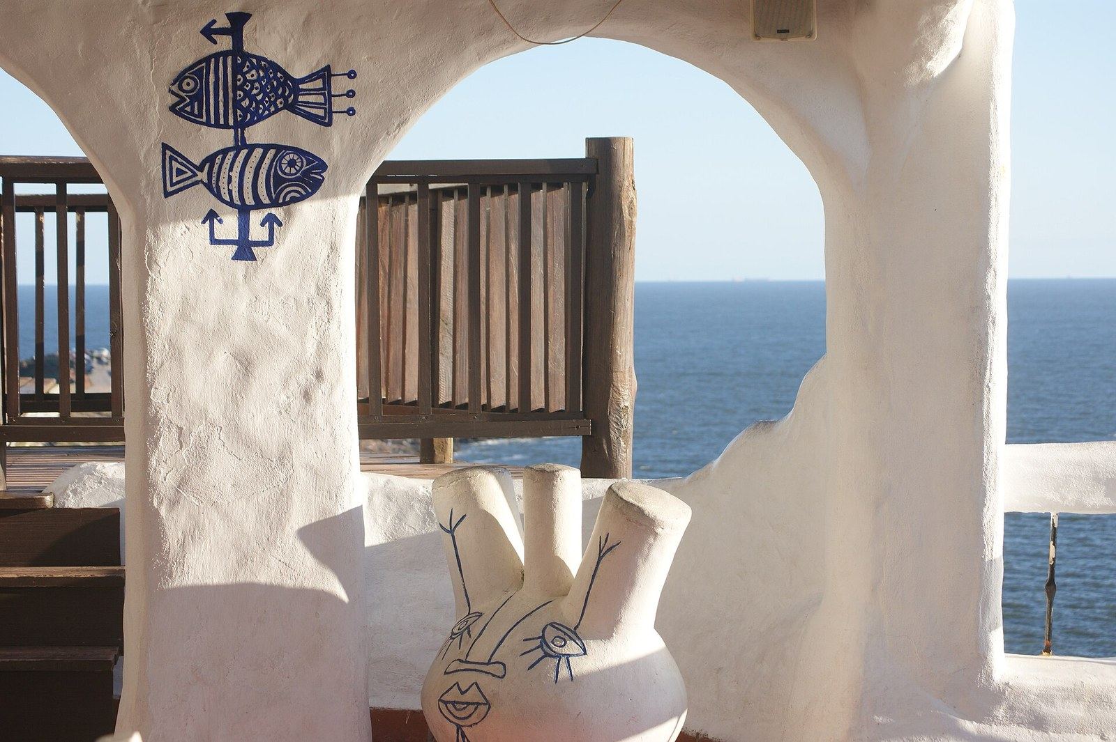 Terraza de Casapueblo con los peces azules dibujados por Carlos Páez Vilaró y una de sus cerámicas, enmarcando el mar de Punta Ballena