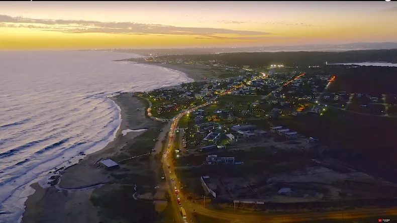 Vista aérea nocturna de La Barra, Punta del Este, con el puente ondulante y las luces del balneario