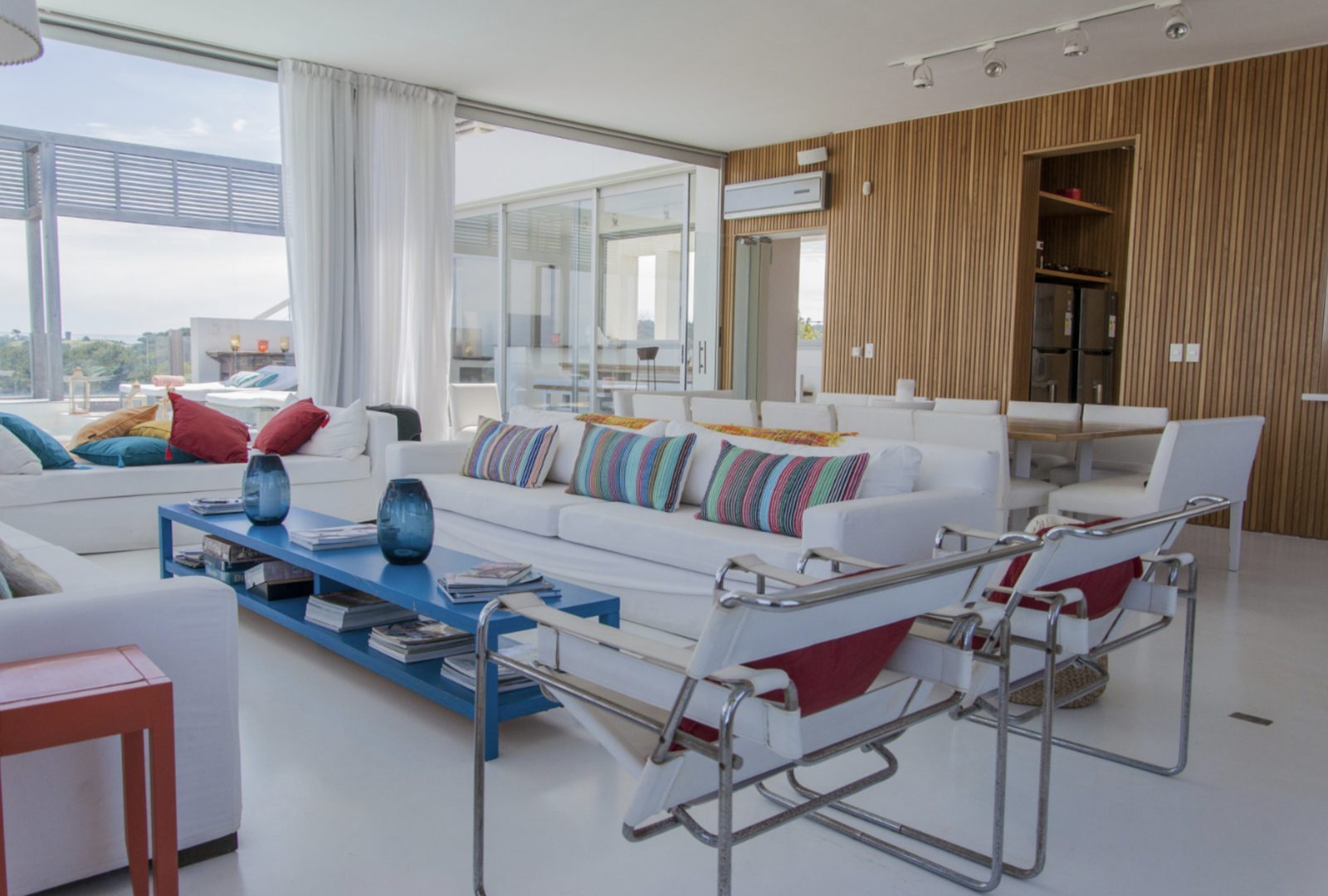Sala luminosa de uma casa em Punta del Este, com parede de madeira e poltronas brancas