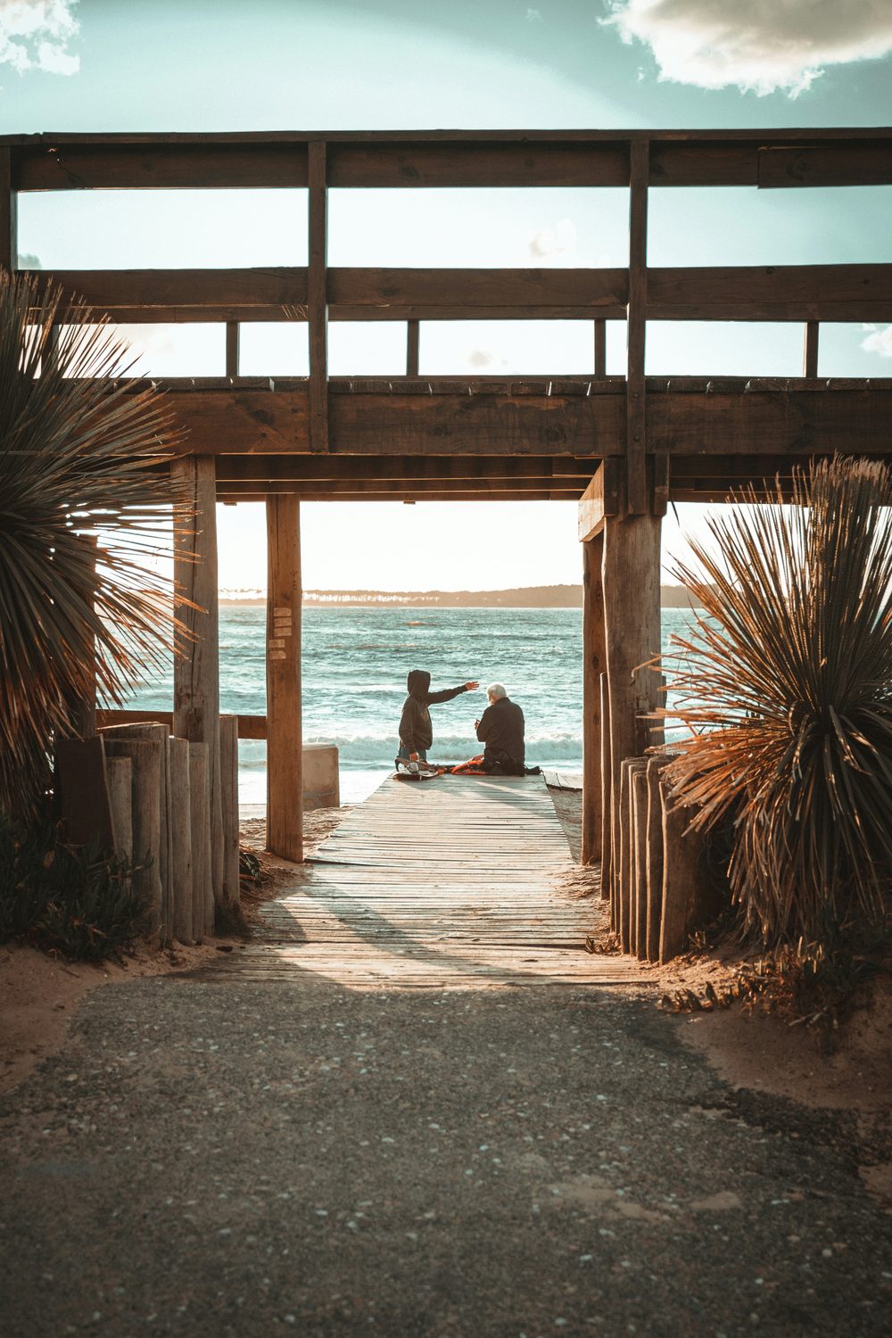 Bajada de madera a la playa de Montoya, con dos personas mirando el mar al atardecer