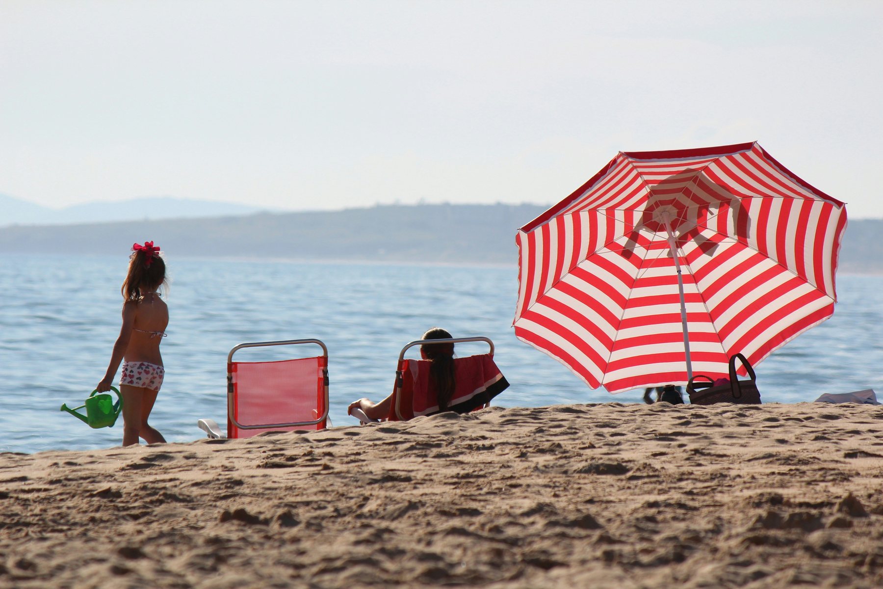 Niña con regadera junto a una sombrilla roja en la Playa Mansa de Punta del Este