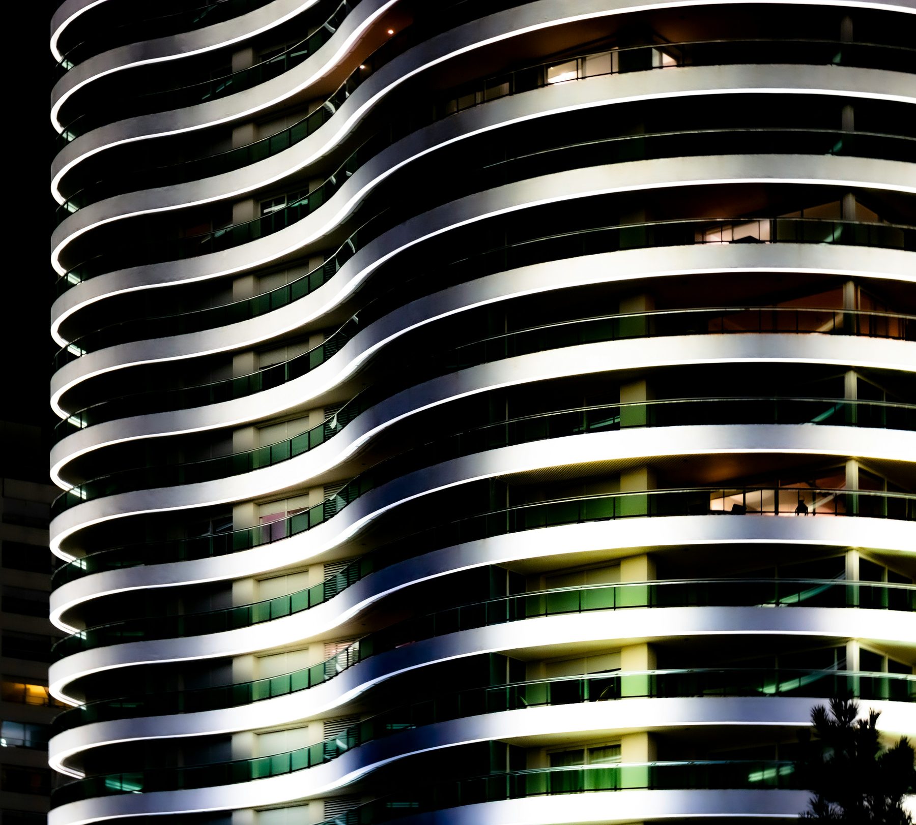 Fachada de una torre de Punta del Este iluminada de noche, con sus balcones curvos